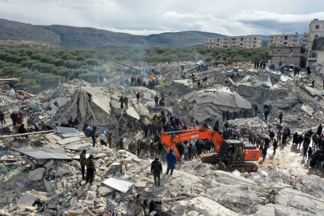 Esta vista aérea mostra residentes em busca de vítimas e sobreviventes em meio aos escombros de prédios desabados após um terremoto na vila de Besnia, perto de Harim, na Síria -