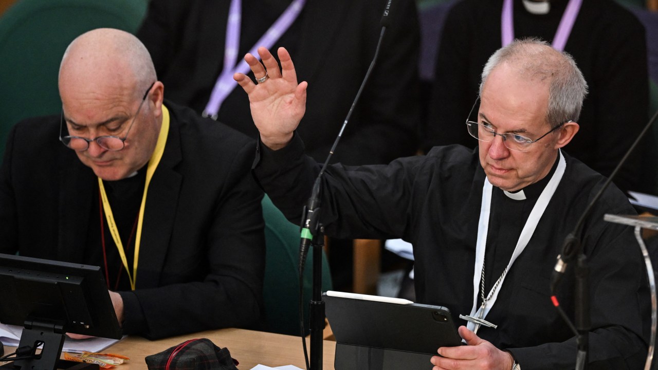Archbishop of Canterbury Justin Welby (R) raises his arm during the voting of a motion during the Church of England Synod, at Church House, in London, on February 7, 2023. (Photo by JUSTIN TALLIS / AFP)
