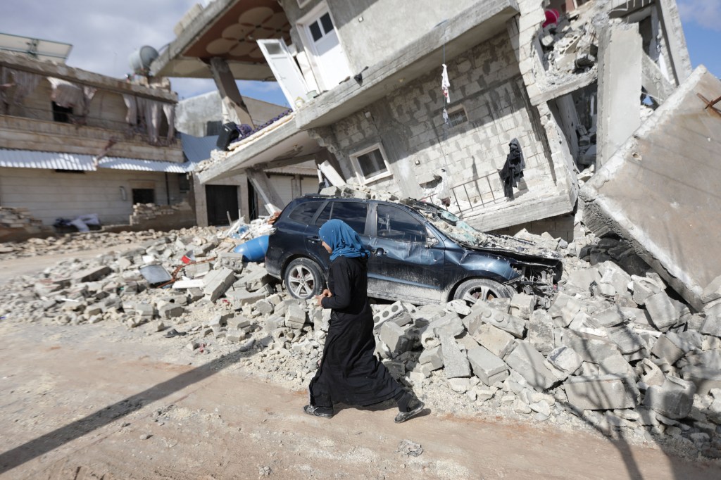 A Syrian woman walks past a half collapsed house in the town of Azaz on the border with Turkey on February 7, 2023, following a deadly earthquake. - The Syrian Red Crescent appealed to Western countries to lift sanctions and provide aid after a powerful earthquake has killed more than 1,600 people across the war-torn country. The 7.8-magnitude quake early the previous day, which has also killed thousands in neighbouring Turkey, led to widespread destruction in both regime-controlled and rebel-held parts of Syria. (Photo by Bakr ALKASEM / AFP)