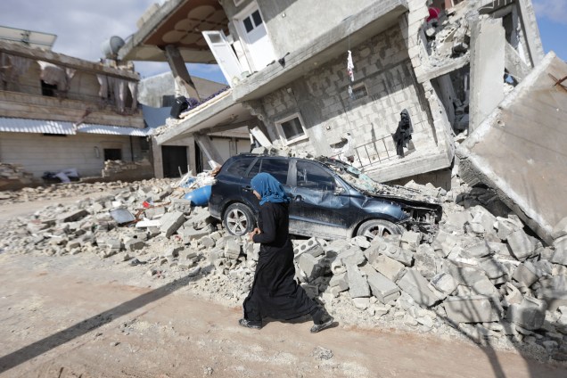 Uma mulher síria passa por uma casa meio desmoronada na cidade de Azaz, na fronteira com a Turquia -