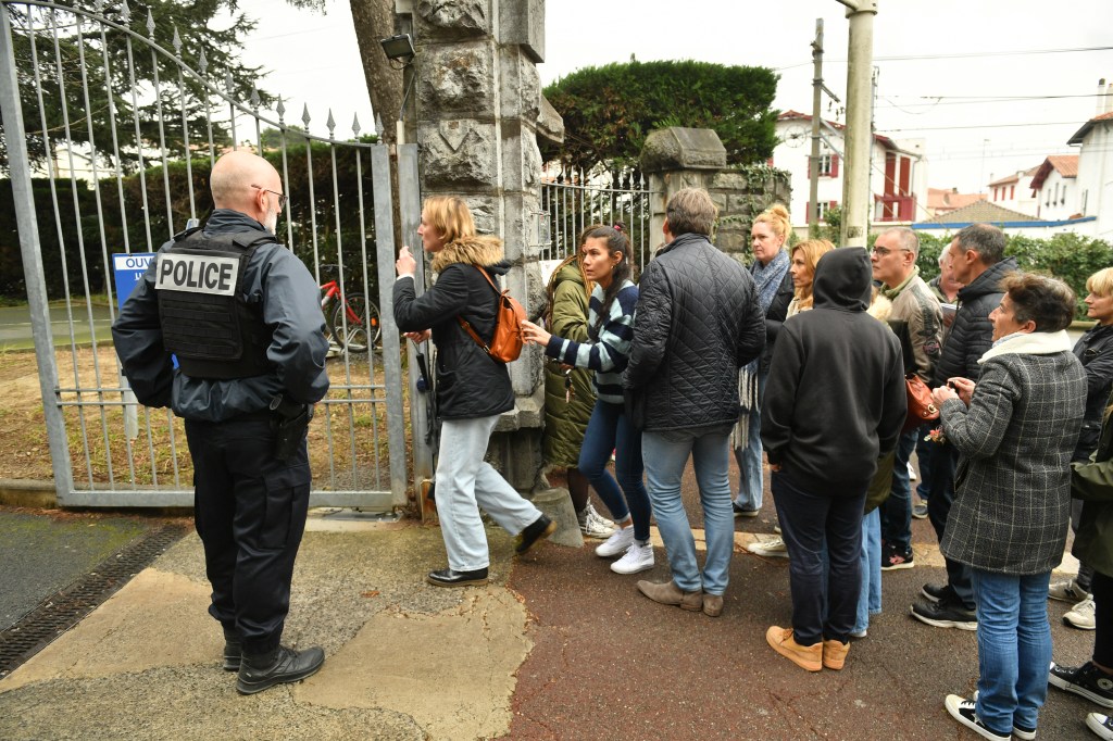 Onlookers gather at the entrance of Saint-Thomas dAquin middle school where a teacher died after being stabbed by a student, in Saint-Jean-de-Luz, southwestern France, on February 22, 2023. - A teacher at a school in southwest France was killed on February 22, in a stabbing attack by a teenage pupil during her class, the regional prosecutor said. The teacher, in her 50s, was teaching a class at the school in the seaside town of Saint-Jean-de-Luz when the pupil attacked her with a knife. (Photo by GAIZKA IROZ / AFP)