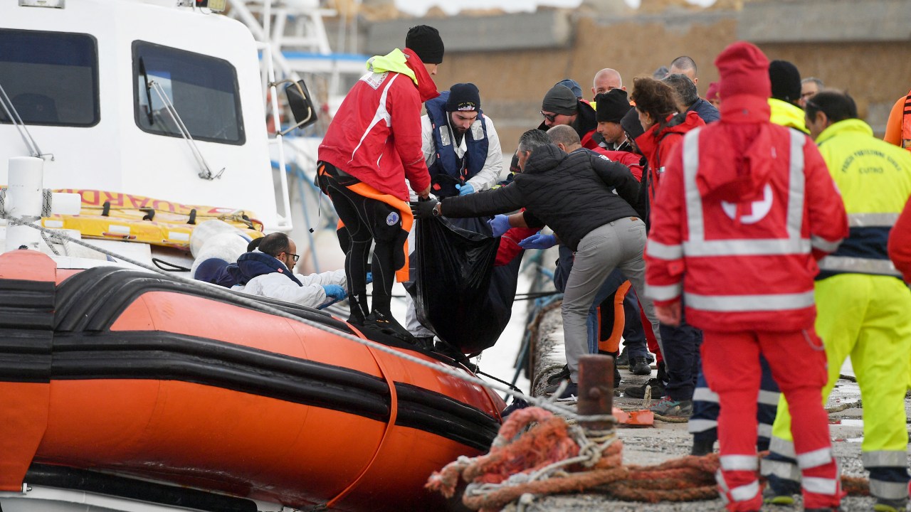 Italian Coast Guard officier carry the body of a deceased migrant in a bag, on February 27, 2023 in the port of Isola di Capo Rizzuto, south of Crotone, after a migrants' boat sank off Italy's southern Calabria region. - At least 59 migrants, including 11 children and a newborn baby, died after their overloaded boat sank early on February 26, 2023 in stormy seas off Italy's southern Calabria region, officials said. (Photo by Alessandro SERRANO / AFP)
