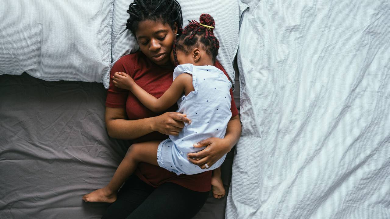 Directly above photo of tired mother with daughter cuddling and napping together on the bedroom.