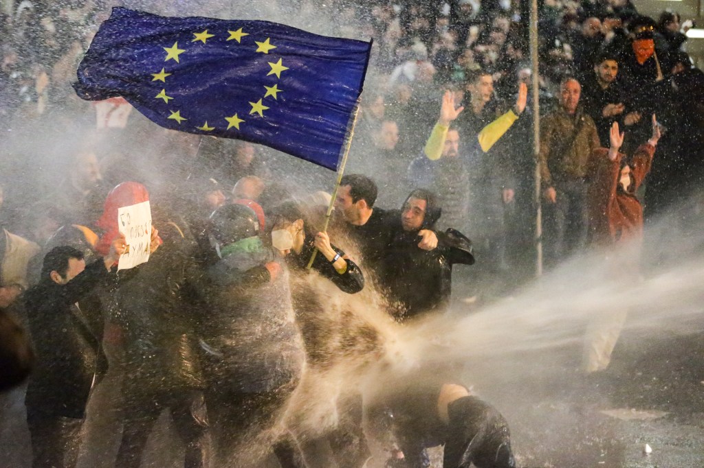 Protesters brandishing a European Union flag brace as they are sprayed by a water canon during clashes with riot police near the Georgian parliament in Tbilisi on March 7, 2023. - Georgian police used tear gas and water cannon against protesters Tuesday as thousands of demonstrators took to the streets in the capital Tbilisi to oppose a controversial "foreign agents" bill. (Photo by AFP)