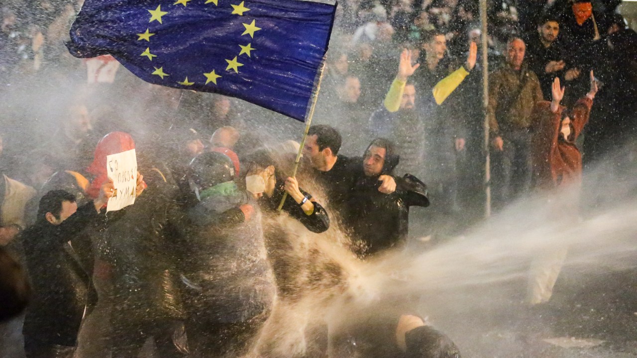 Protesters brandishing a European Union flag brace as they are sprayed by a water canon during clashes with riot police near the Georgian parliament in Tbilisi on March 7, 2023. - Georgian police used tear gas and water cannon against protesters Tuesday as thousands of demonstrators took to the streets in the capital Tbilisi to oppose a controversial "foreign agents" bill. (Photo by AFP)