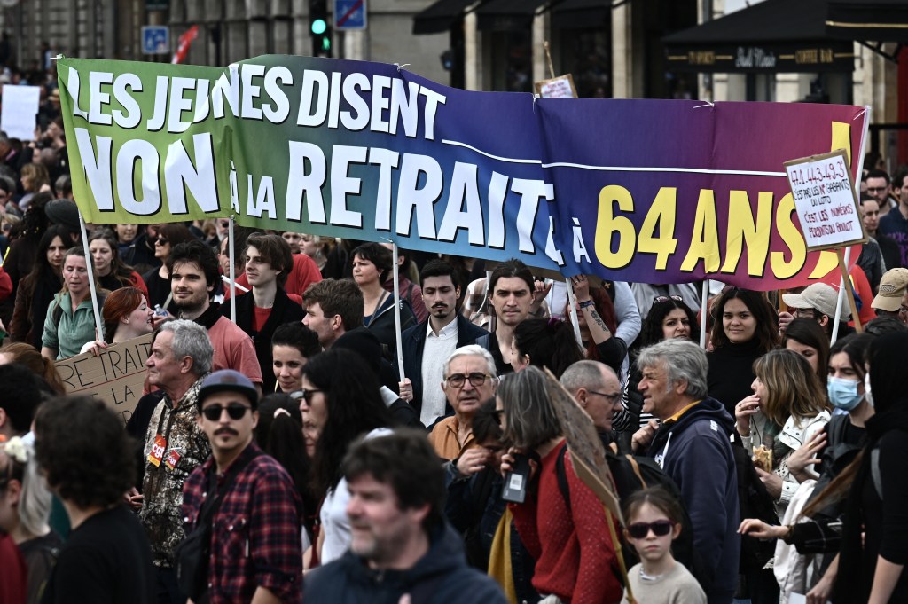 Protesters gather, holding a banner which reads as "Young people say no to pension at 64 year-old", as they take part in a demonstration on a national action day, a week after the government pushed a pensions reform through parliament without a vote, using the article 49.3 of the constitution, in Bordeaux, western France, on March 23, 2023. - French President defiantly vowed to push through a controversial pensions reform on March 22, 2023, saying he was prepared to accept unpopularity in the face of sometimes violent protests. (Photo by Philippe LOPEZ / AFP)