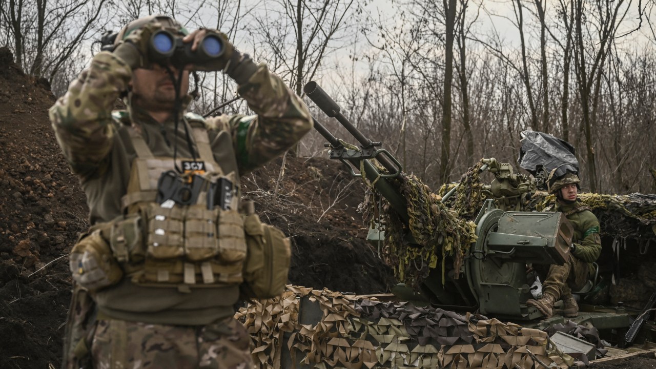 A Ukrainian serviceman (L) looks on with binoculars next to another (R) sitting on an anti-air gun near Bakhmut, on March 24, 2023. (Photo by Aris Messinis / AFP)