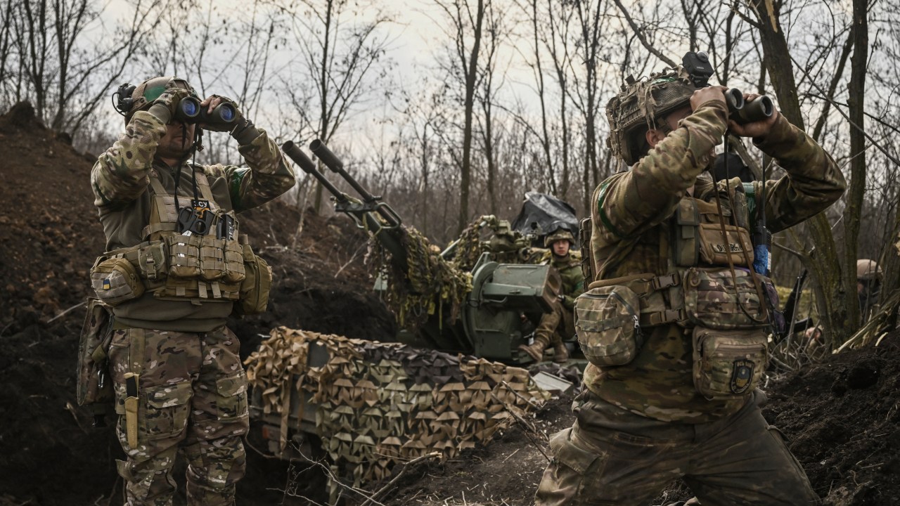 Ukrainian servicemen (L and R) look on with binoculars next to another (C) sitting on an anti-air gun near Bakhmut, on March 24, 2023. (Photo by Aris Messinis / AFP)