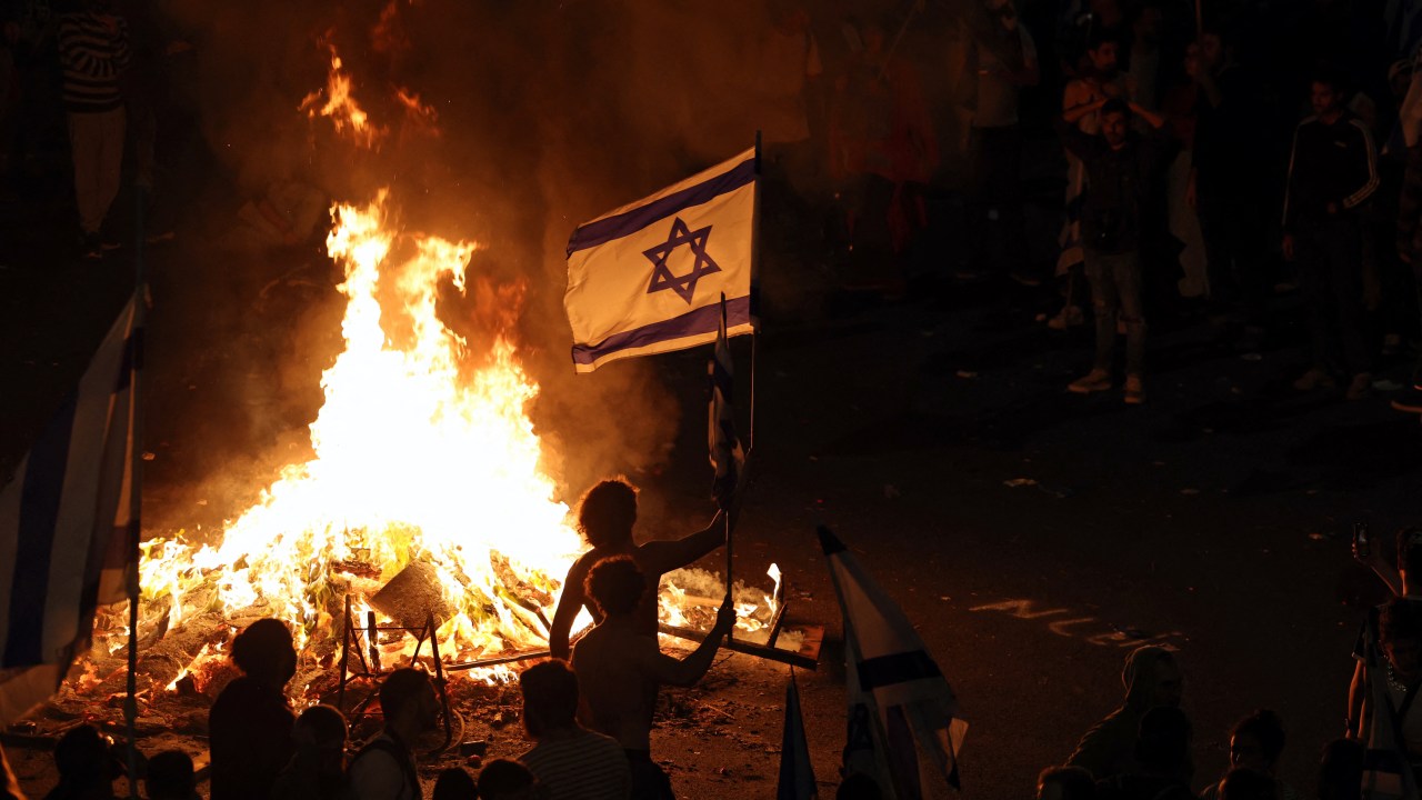 Protesters block a road and hold national flags as they gather around a bonfire during a rally against the Israeli government's judicial reform in Tel Aviv, Israel on March 27, 2023. - Israeli Prime Minister Benjamin Netanyahu on March 26, 2023 fired Defence Minister Yoav Galant a day after he broke ranks, citing security concerns in calling for a pause to the government's controversial judicial reforms. On a day when 200,000 people took to the streets of Tel Aviv to protest the reforms, Galant -- who had been a staunch Netanyahu ally -- on Saturday said "we must stop the legislative process" for a month in view of its divisiveness. (Photo by AHMAD GHARABLI / AFP)