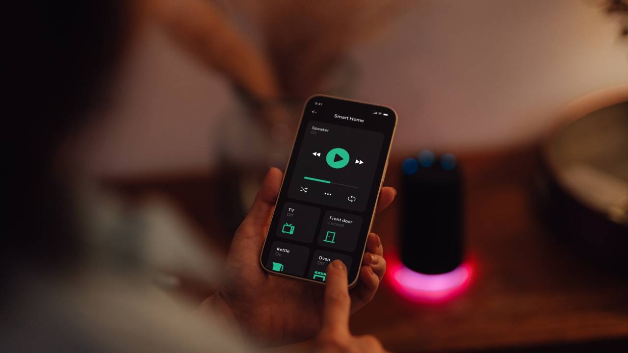Over the shoulder view of young Asian woman using smartphone to play music on smart speaker of a modern smart home. Smart home technology concept. Smart living. Lifestyle and technology.
