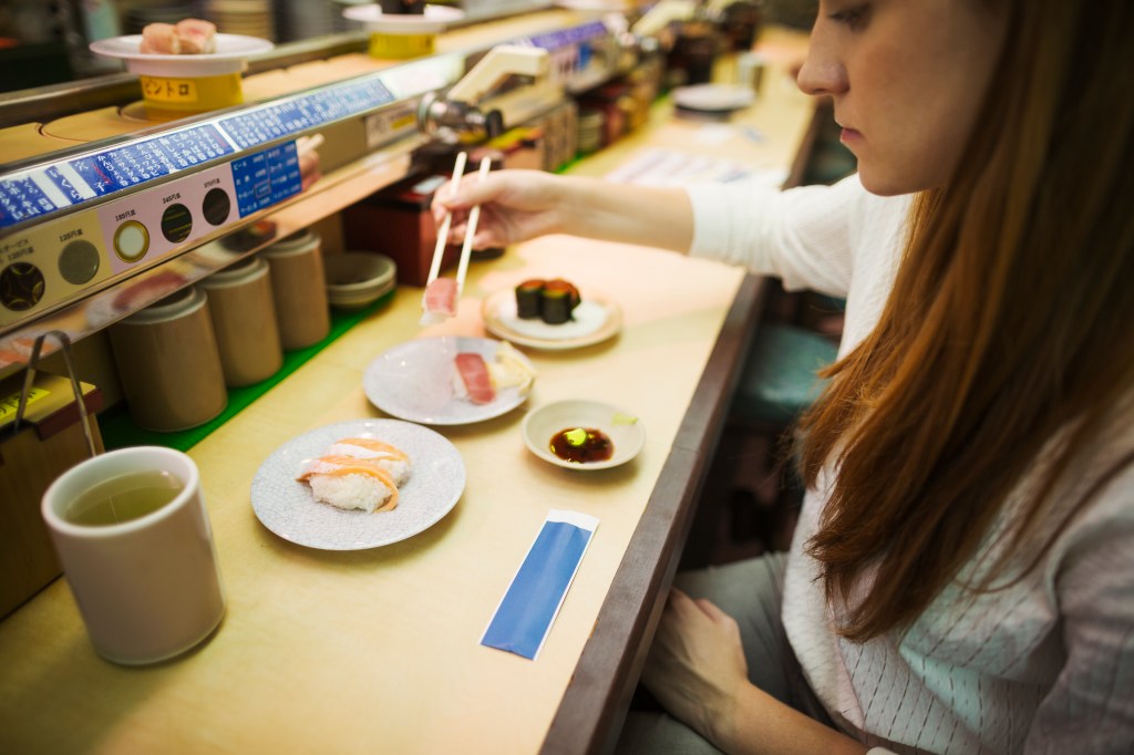 High angle view of woman eating in a sushi bar, with sushi train, Kaiten-zushi.