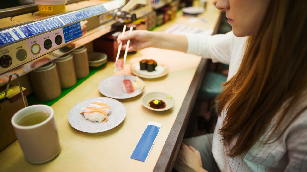High angle view of woman eating in a sushi bar, with sushi train, Kaiten-zushi.