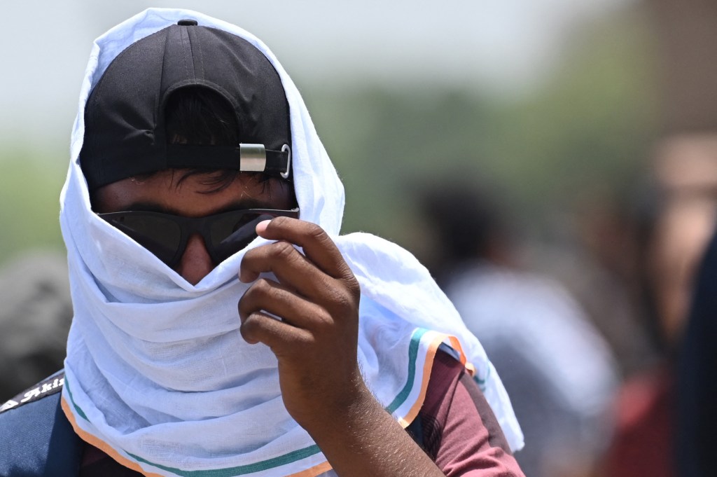 A man uses a scarf to shelter from the heat during a hot day in New Delhi on April 19, 2023. (Photo by Arun SANKAR / AFP)