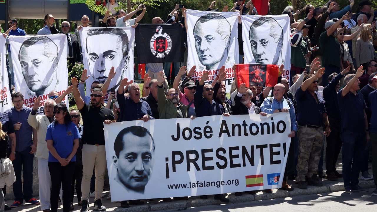 Fascism sympathizers performing the fascist salute hold banners remembering the founder of Falange, Jose Antonio Primo de Rivera, outside the San Isidro cemetery in Madrid, where the fascist politician will be buried following his exhumation from the Valle de los Caidos basilica, officially named Valle de Cuelgamuros, on April 24, 2023. - Experts were today exhuming the remains of the founder of Spain's fascist Falange party, Jose Antonio Primo de Rivera, from a grandiose basilica, where the body of former dictator Francisco Franco once lay, ahead of their removal to a low-key family grave. Jose Antonio Primo de Rivera founded the Falange party in 1933, which became one of the pillars of Francisco Franco's brutal regime, along with the military and Spain's Roman Catholic Church. (Photo by Thomas COEX / AFP)