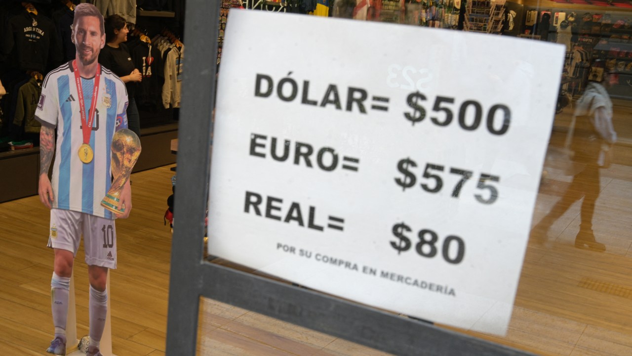 A sign with exchange currency values of the unofficial so-called "Blue Dollar" of the parallel "blue" market, is displayed in the window of a store in Buenos Aires near a cardboard figure of Argentine football star Lionel Messi, on April 26, 2023. - Argentina's government on April 25, 2023, accused the country's rightwing opposition of fueling a dramatic erosion of the peso against the US dollar, and ordered an investigation. The slide started last week after several days of pressure on the peso in a period of pre-election uncertainty in a country with exchange controls in place to try to limit the effects of a financial crisis and rampant inflation. (Photo by Juan MABROMATA / AFP)