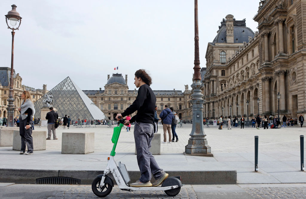 PARIS, FRANCE - MARCH 29: A man rides a Lime electric scooter in front of the Louvre pyramid and the Louvre museum on March 29, 2023 in Paris, France. The Mayor of Paris, Anne Hidalgo is organizing a local referendum on Sunday April 2, 2023 to ask Parisians if they want to keep self-service electric scooters in the capital. (Photo by Chesnot/Getty Images)