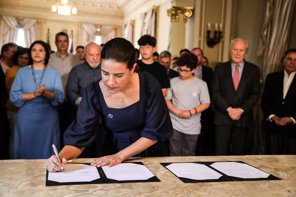 A governadora de Pernambuco, Raquel Lyra (PSDB), assina documento em evento com o presidente Lula (ao fundo)