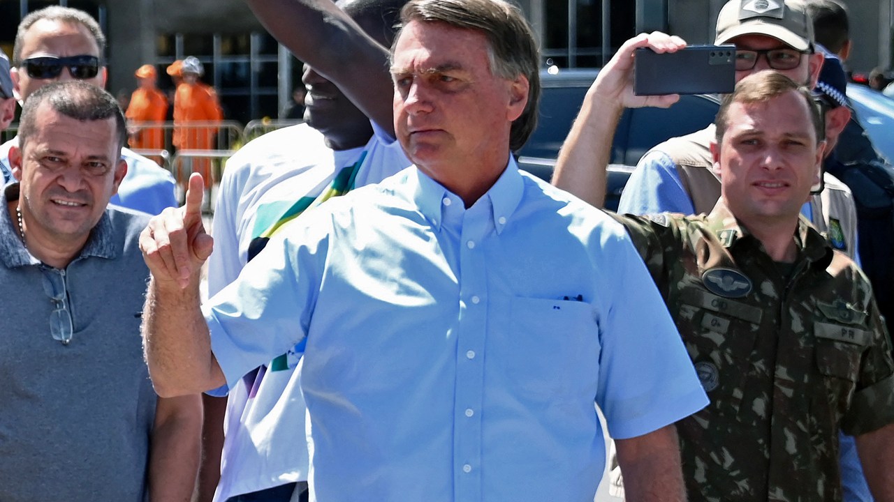 (FILES) Brazilian President Jair Bolsonaro (C), accompanied by personal assistant army officer Mauro Cid (R), greets supporters cheering for him and his controversial ally, deputy Daniel Silveira, who Bolsonaro pardoned after the Supreme Court had sentenced him to prison time for his role leading a movement calling for the court to be overthrown, in Brasilia on May Day, on May 1, 2022. - Police in Brazil searched ex-president Jair Bolsonaro's home on May 3, 2023, as part of an investigation into allegations of falsifying COVID-19 vaccination certificates. The far-right ex-president (2019-2022), who faced widespread criticism for his unorthodox handling of the pandemic, has repeatedly said he is not vaccinated against COVID-19 .Media reports said police had arrested a top Bolsonaro aide, army officer Mauro Cid. (Photo by EVARISTO SA / AFP)