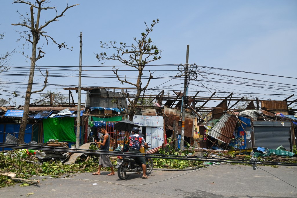 People pass damaged structures in Sittwe in Myanmar's Rakhine state on May 15, 2023, after cyclone Mocha made landfall. Cyclone Mocha made landfall on May 14 between Cox's Bazar in Bangladesh and Myanmar's Sittwe carrying winds of up to 195 kilometres (120 miles) per hour, the biggest storm to hit the Bay of Bengal in more than a decade. (Photo by Sai Aung MAIN / AFP)