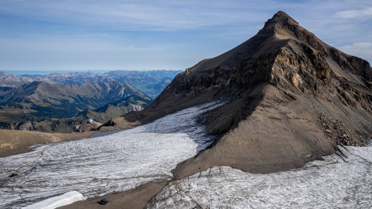 (FILES) This aerial picture taken on September 13, 2022 at Glacier 3000 resort above Les Diablerets shows the Tsanfleuron pass free of the ice that covered it for at least 2,000 years next to blankets (L) covering snow from the last winter season to prevent it from melting. (Photo by Fabrice COFFRINI / AFP)