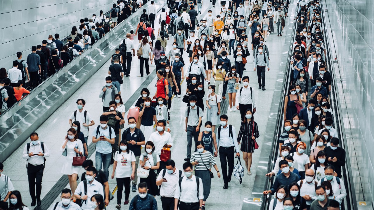 Crowd of busy commuters with protective face mask walking through platforms at subway station during office peak hours in the city