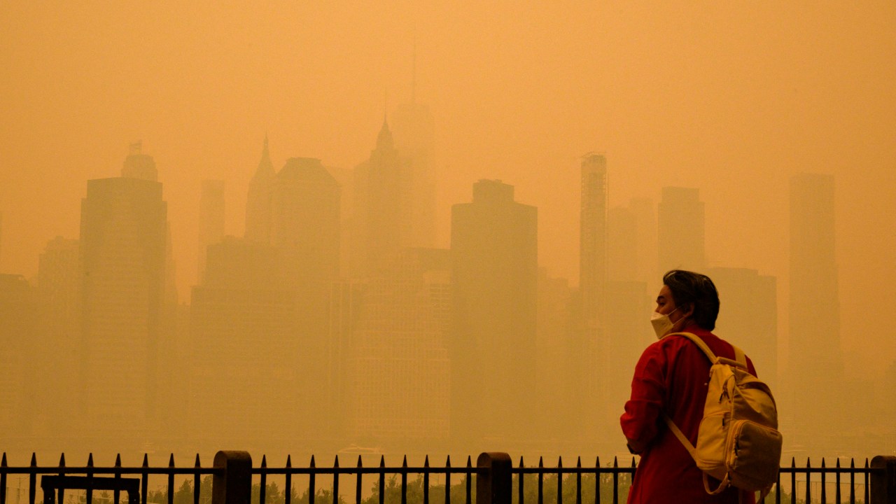 A person wears a face mask as smoke from wildfires in Canada cause hazy conditions in New York City on June 7, 2023. An orange-tinged smog caused by Canada's wildfires shrouded New York on Wednesday, obscuring its famous skyscrapers and causing residents to don face masks, as cities along the US East Coast issued air quality alerts. (Photo by ANGELA WEISS / AFP)