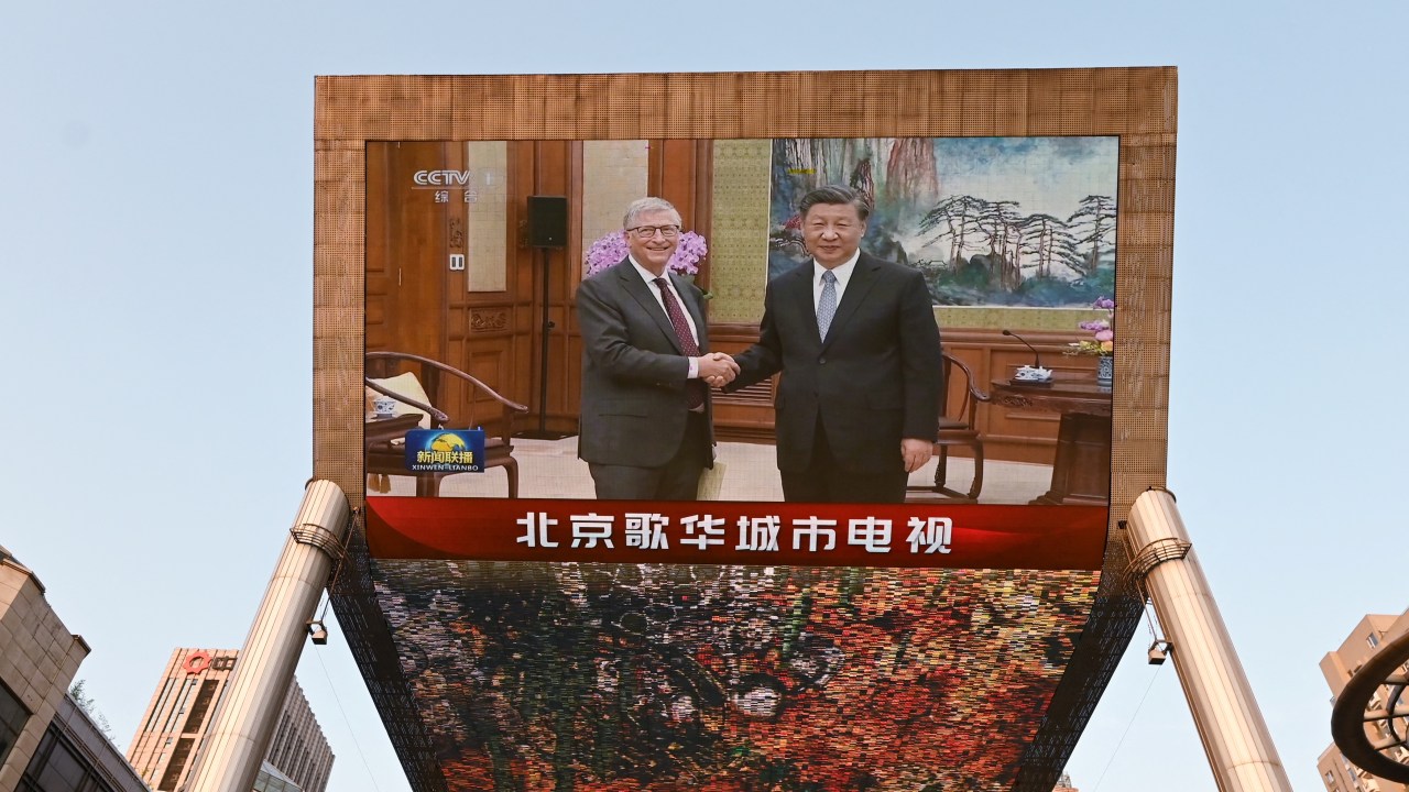 A China Central Television news broadcast shows footage of Microsoft co-founder Bill Gates (L) meeting with Chinese President Xi Jinping, on a giant screen outside a shopping mall in Beijing on June 16, 2023. President Xi Jinping told his "old friend" Bill Gates on June 16 that China had always placed its hopes in the American people, after the Microsoft co-founder's foundation pledged $50 million to help Chinese efforts to battle disease. (Photo by GREG BAKER / AFP)