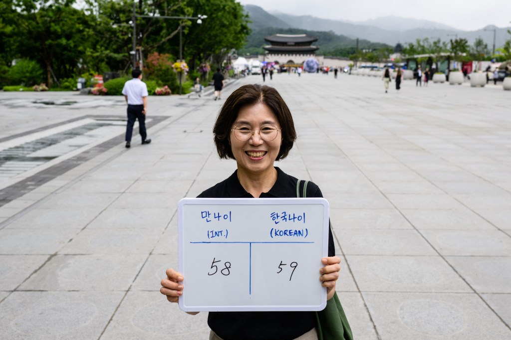 In this picture taken in Seoul on June 21, 2023, Lee Jung-hee, poses with a whiteboard showing her international age, 58, and Korean age, 59. From June 28, 2023 South Korea will use the international system that calculates age according to a person's actual date of birth, meaning everyone will officially become a year or two younger. "For people like me, who were supposed to turn 60 next year, it makes you feel like you're still young," Lee told AFP. (Photo by ANTHONY WALLACE / AFP) / To go with "SKorea-politics-culture-age", FOCUS by Cat BARTON