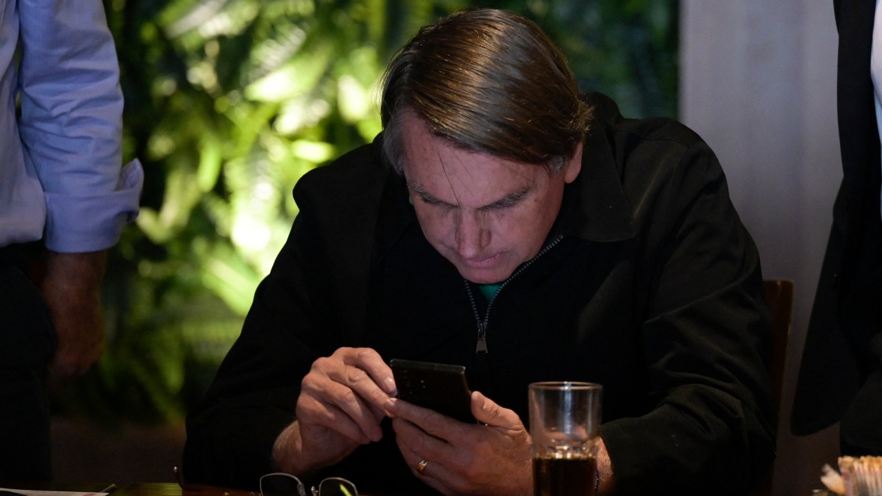 Former Brazilian President Jair Bolsonaro checks his phone before addressing members of the media in Belo Horizonte, Minas Gerais state, Brazil, on June 30, 2023. Brazil's Superior Electoral Tribunal on Friday reached the majority it needs to bar far-right former president Jair Bolsonaro from politics for eight years over his unfounded claims against the voting system. (Photo by DOUGLAS MAGNO / AFP)