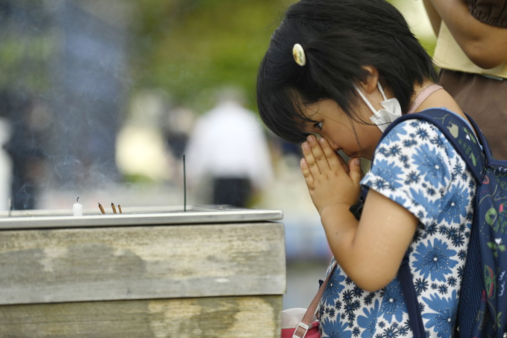HIROSHIMA, JAPAN - AUGUST 05: A little child prays in front of a cenotaph for the victims of the world's first atomic bombing, on which it is written 'May all souls here rest in peace because we will not repeat that' in Hiroshima, Japan, on August 05, 2022. Japan prepares for the ceremony in Peace Memorial Park to commemorate the 77th anniversary of the atomic bomb tragedy in Hiroshima. During World War II, on August 6, 1945, the first atomic bomb in the world history was dropped on Hiroshima by the USA, which caused the instant death of an estimated 70,000 people and the death of thousands from the effects of radiation in the following years. (Photo by David MAREUIL/Anadolu Agency via Getty Images)