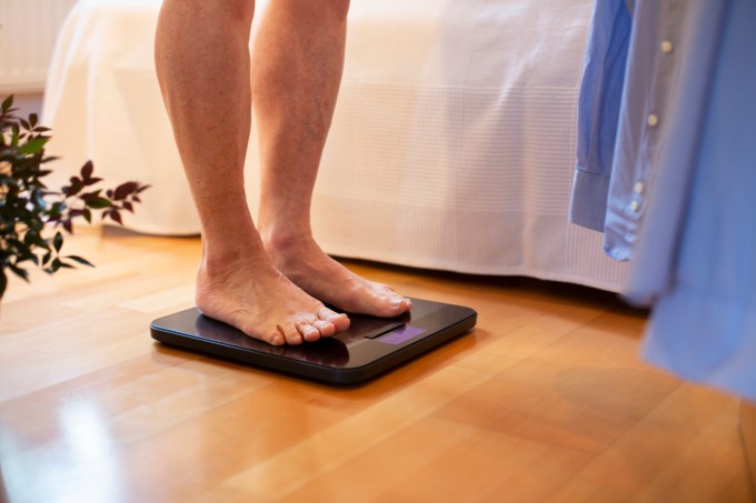 Senior man standing on weight scale, low section