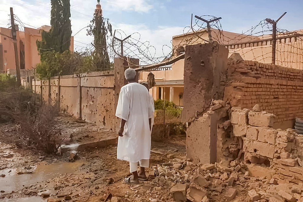 A man walks through rubble by a bullet-riddled fence with barbed-wire, in the aftermath of clashes and bombardment in the Ombada suburb on the western outskirts of Omdurman, the twin-city of Sudan's capital, on July 4, 2023. Heavy fighting raged on July 4 across the Sudanese capital where witnesses reported a fighter-jet being shot down and artillery and machine gun fire rocking several neighbourhoods. (Photo by AFP)