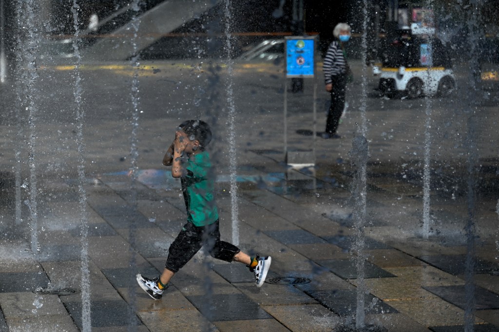 A boy runs past jets of water of a fountain amid hot weather in Beijing on July 5, 2023. (Photo by Pedro PARDO / AFP)