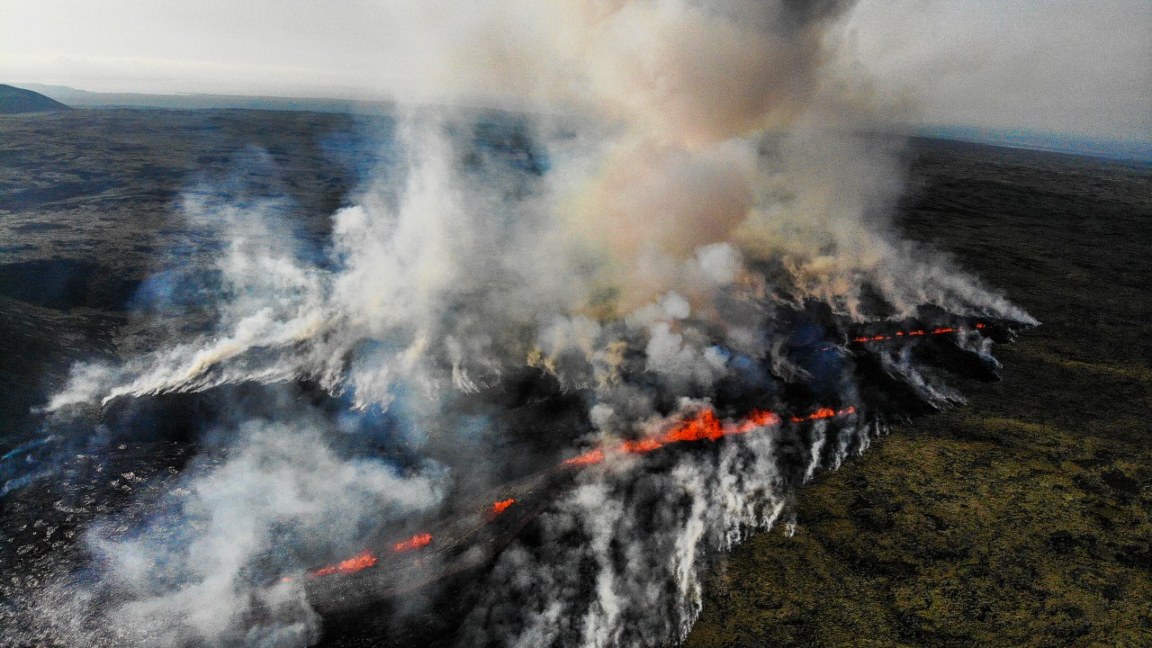 This aerial photograph taken on July 10, 2023 shows smoke billowing from flowing lava during an volcanic eruption near Litli Hrutur, south-west of Reykjavik in Iceland. A volcanic eruption started on July 10, 2023 around 30 kilometres (19 miles) from Iceland's capital Reykjavik, the country's meteorological office said, marking the third time in two years that lava has gushed out in the area. "The eruption is taking place in a small depression just north of Litli Hrutur, from which smoke is escaping in a north-westerly direction," the office said. Footage circulating in the local media shows a massive cloud of smoke rising from the ground as well as a substantial flow of lava. (Photo by Kristinn Magnusson / AFP) / Iceland OUT