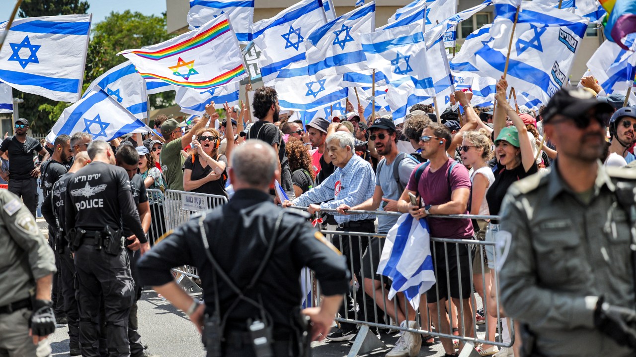 Israeli police stand alert as anti-government demonstrators gather behind a barrier during a protest in Tel Aviv on July 11, 2023. Protesters blocked roads across Israel on July 11 hours after parliament adopted in a first reading a key clause of the government's judicial overhaul package which opponents say threatens democracy. (Photo by AHMAD GHARABLI / AFP)