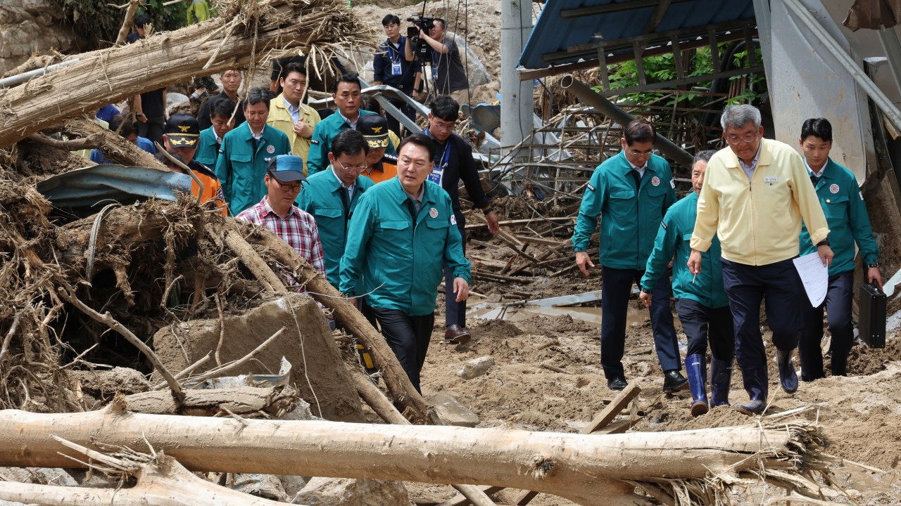 South Korea's President Yoon Suk Yeol (C) walks past piles of fallen trees at a village, where more than a third of houses were damaged in landslides and two people remain missing, in Yecheon on July 17, 2023. South Korea's president vowed on July 17, to "completely overhaul" the country's approach to extreme weather from climate change, after at least 40 people were killed by recent flooding and landslides during monsoon rains. (Photo by YONHAP / AFP) / - South Korea OUT / NO ARCHIVES - REPUBLIC OF KOREA OUT RESTRICTED TO SUBSCRIPTION USE