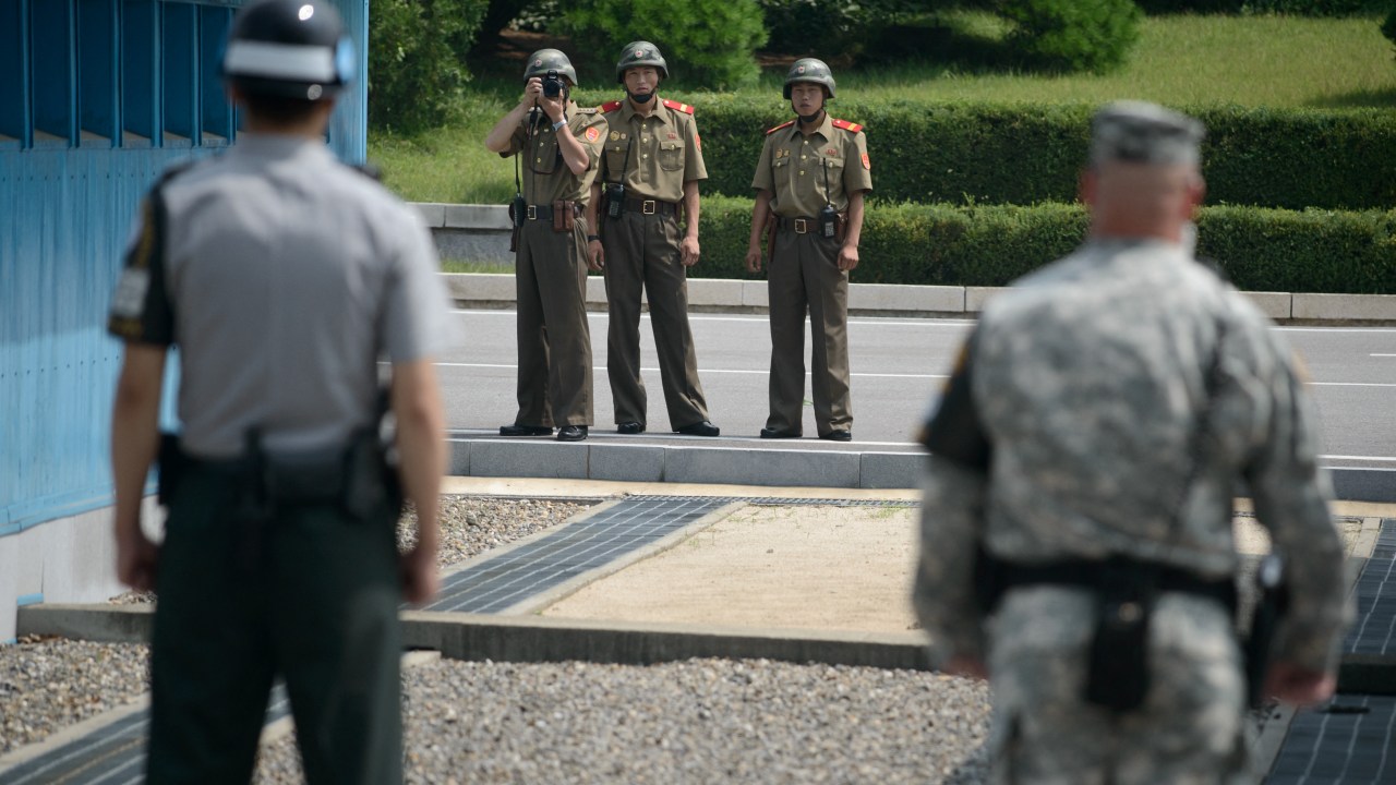 (FILES) North Korean soldiers (C) take photos towards a South Korean soldier (L) and a US soldier (R) standing before the military demarcation line (lower C) seperating North and South Korea within the Joint Security Area (JSA) at Panmunjom on July 27, 2014. A United States national entered North Korea during a tour of the heavily-fortified border and is believed to have been detained, the United Nations Command said July 18, 2023. (Photo by Ed JONES / AFP)