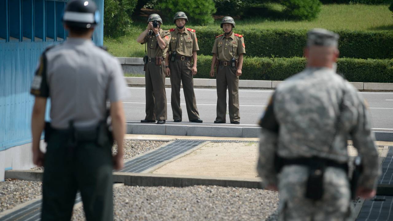 (FILES) North Korean soldiers (C) take photos towards a South Korean soldier (L) and a US soldier (R) standing before the military demarcation line (lower C) seperating North and South Korea within the Joint Security Area (JSA) at Panmunjom on July 27, 2014. A United States national entered North Korea during a tour of the heavily-fortified border and is believed to have been detained, the United Nations Command said July 18, 2023. (Photo by Ed JONES / AFP)