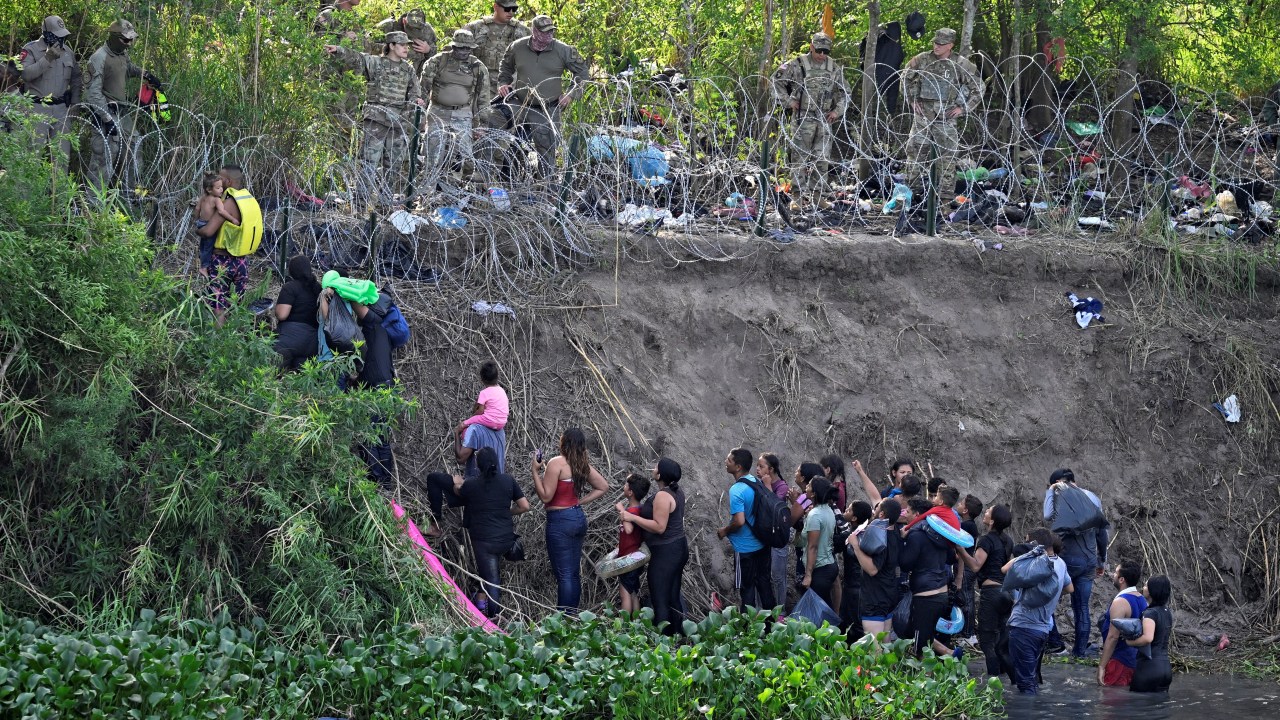 Imigrantes que cruzaram o rio Bravo (Rio Grande nos Estados Unidos) são detidos por membros da Guarda Nacional dos EUA, que reforçam uma cerca de arame farpado na fronteira EUA-México. 10/05/2023