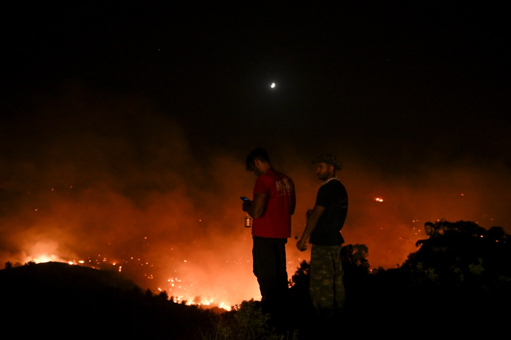 People watch the fires near the village of Malona in the Greek island of Rhodes on July 23, 2023. Tens of thousands of people fled wildfires on the Greek island of Rhodes on July 23, 2023, as terrified tourists scrambled to get home. Firefighters tackled blazes that erupted in peak tourism season, sparking the country's largest-ever wildfire evacuation -- and leaving flights and holidays cancelled. (Photo by SPYROS BAKALIS / AFP)