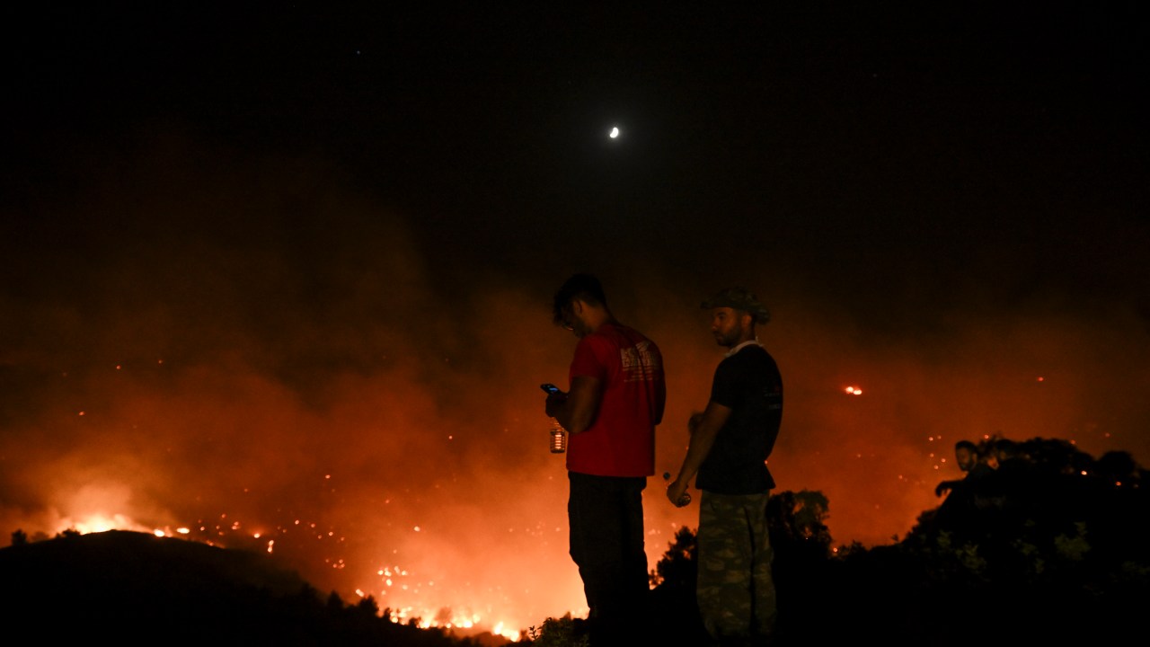 People watch the fires near the village of Malona in the Greek island of Rhodes on July 23, 2023. Tens of thousands of people fled wildfires on the Greek island of Rhodes on July 23, 2023, as terrified tourists scrambled to get home. Firefighters tackled blazes that erupted in peak tourism season, sparking the country's largest-ever wildfire evacuation -- and leaving flights and holidays cancelled. (Photo by SPYROS BAKALIS / AFP)
