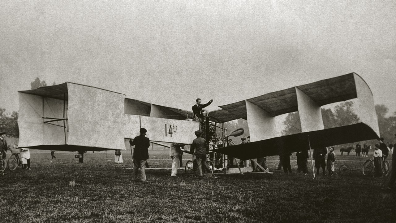AMPLA DIVULGAÇÃO - Santos Dumont aparece no alto do 14 Bis: voo com plano e festa