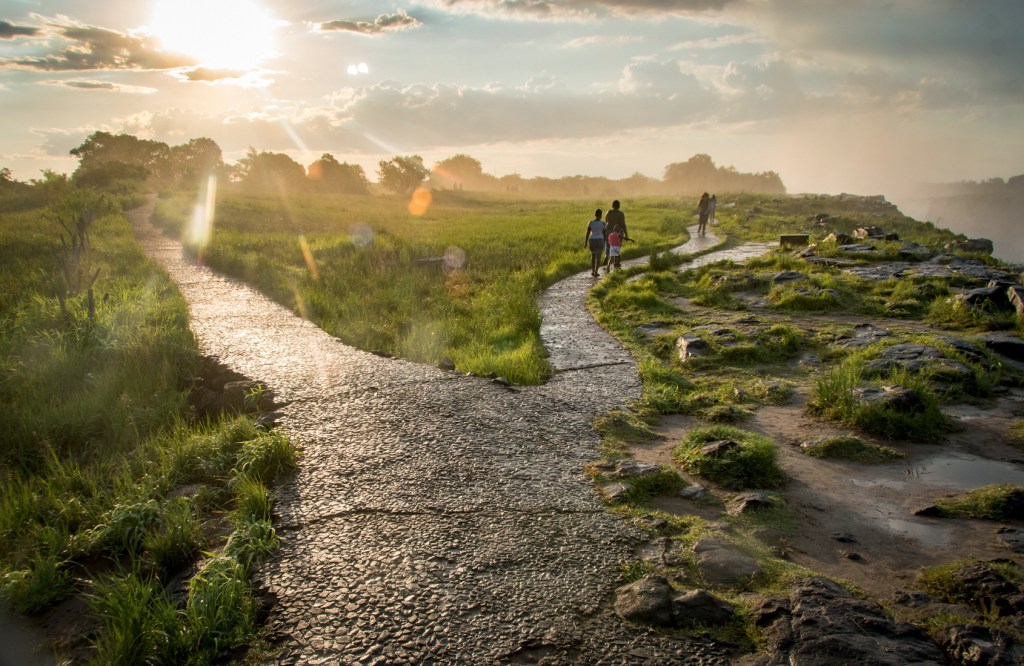 Tourists walk along a pathway at Victoria Falls which spray mist into the air contributing to the areas thick, lush vegetation. Mosi-oa-Tunya National Park, Zimbabwe VICTORIA FALLS, ZIMBÁBUE - O Parque Nacional Mosi-oa-Tunya, na fronteira com a Zâmbia, é uma das maiores quedas-d'água do mundo. Os viajantes passeiam e, simultaneamente, entendem o zelo com a fauna, composta de animais como elefantes e búfalos
