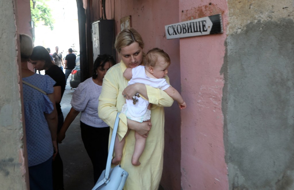 A young woman carries a baby as she walks past sign "Shelter" during airstrike alarm near Transfiguration Cathedral damaged as a result of a missile strike in Odesa the day before, prior service on July 24, 2023, amid the Russian invasion of Ukraine. Ukraine on Sunday said 19 people, including four children, were wounded in a Russian overnight missile attack on Odesa that also killed one person. (Photo by Oleksandr GIMANOV / AFP)