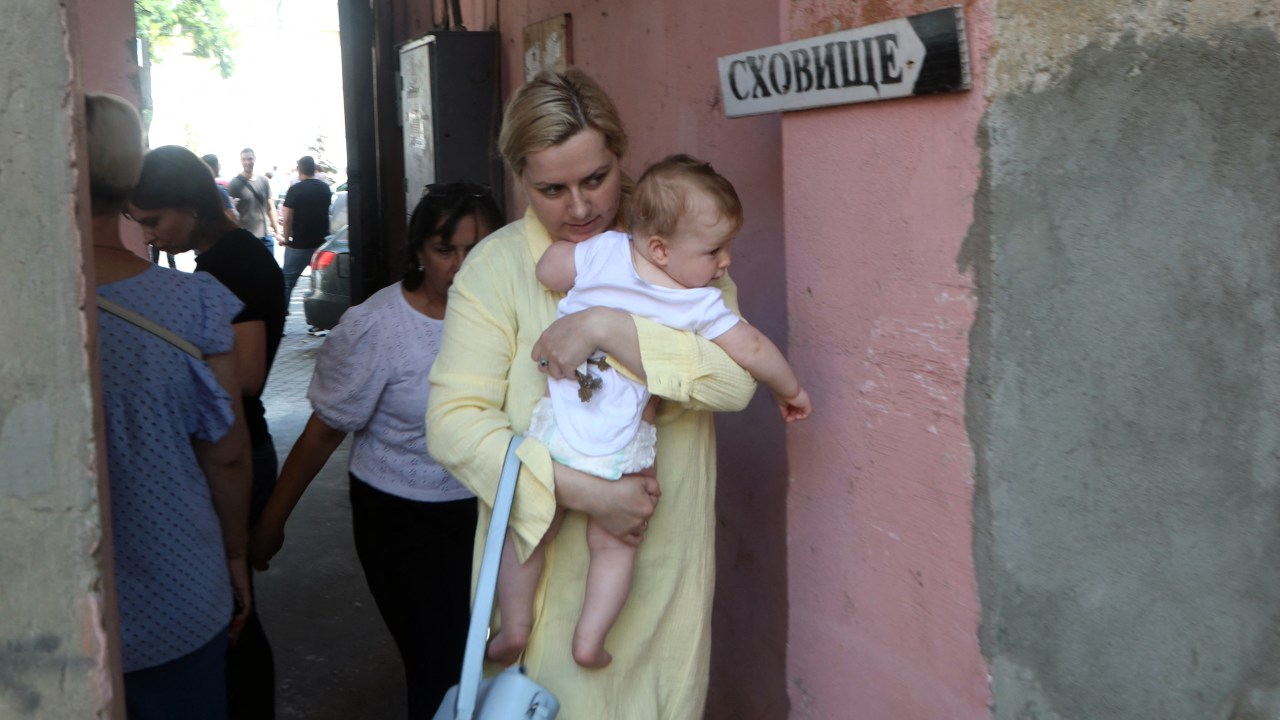 A young woman carries a baby as she walks past sign "Shelter" during airstrike alarm near Transfiguration Cathedral damaged as a result of a missile strike in Odesa the day before, prior service on July 24, 2023, amid the Russian invasion of Ukraine. Ukraine on Sunday said 19 people, including four children, were wounded in a Russian overnight missile attack on Odesa that also killed one person. (Photo by Oleksandr GIMANOV / AFP)