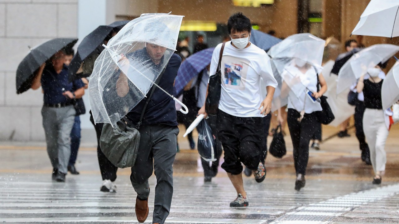 Pedestrians try to shield from wind and rain as they cross the street in front of Osaka Station on August 15, 2023, as Tropical Storm Lan hit the main island of Honshu overnight. The tropical storm, downgraded from a typhoon, slammed into Japan's main island early on August 15, bringing violent gusts and downpours that have already caused rivers to surge and prompted landslide warnings. (Photo by JIJI Press / AFP) / Japan OUT
