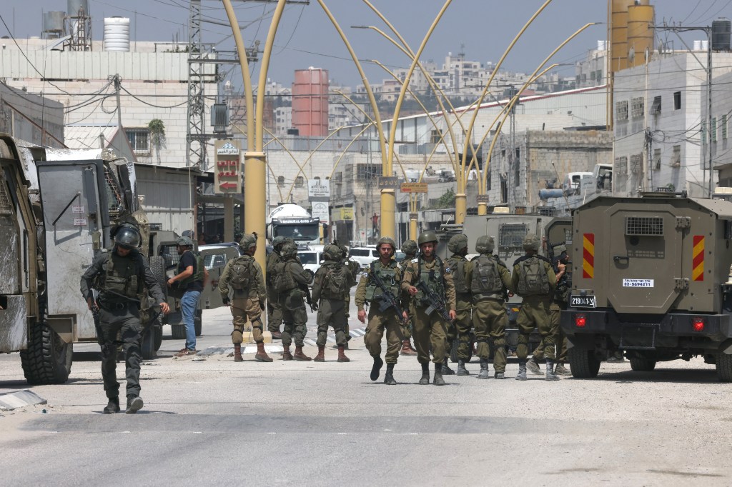 Members of Israeli security forces block a road leading to the site of a reported attack south of Hebron in the occupied West Bank, on August 21, 2023. An Israeli woman was shot dead and another man wounded in a suspected shooting attack when they were driving near Hebron on August 21, medics and the army said. (Photo by HAZEM BADER / AFP)