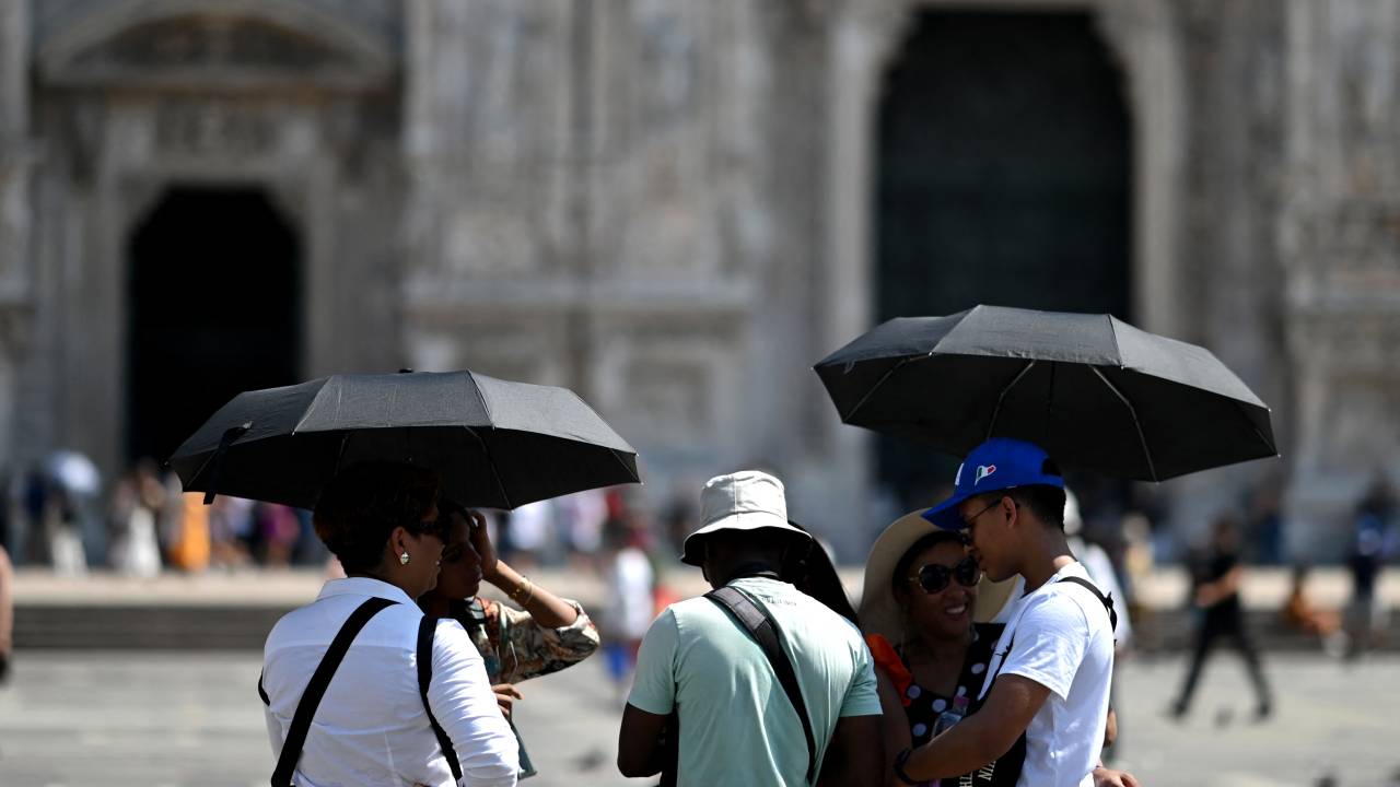 Tourists protect themselves from the heat with umbrellas in front of the Duomo Cathedral in the touristic center of Milan during a late summer heatwave on August 21, 2023. (Photo by GABRIEL BOUYS / AFP)