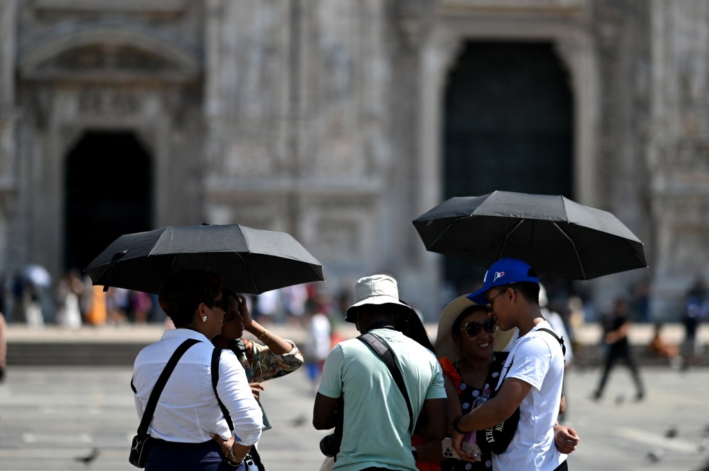 Tourists protect themselves from the heat with umbrellas in front of the Duomo Cathedral in the touristic center of Milan during a late summer heatwave on August 21, 2023. (Photo by GABRIEL BOUYS / AFP)