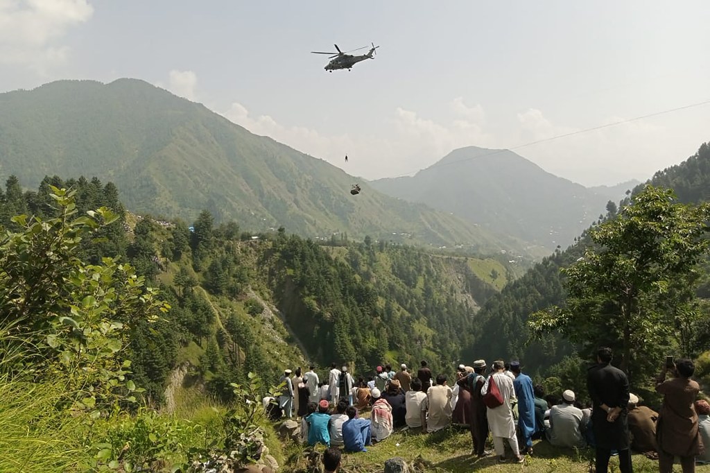 People watch as an army soldier slings down from a helicopter during a rescue mission to recover students stuck in a chairlift in Pashto village of mountainous Khyber Pakhtunkhwa province, on August 22, 2023. Six children and two adults were suspended inside a cable car dangling over a deep valley in Pakistan for several hours on August 22, as a military helicopter hovered nearby. (Photo by AFP) / CORRECTION: The erroneous mention[s] appearing in the metadata of this photo by - has been modified in AFP systems in the following manner: [Stringer] instead of [Prateek Kumar]. Please immediately remove the erroneous mention[s] from all your online services and delete it (them) from your servers. If you have been authorized by AFP to distribute it (them) to third parties, please ensure that the same actions are carried out by them. Failure to promptly comply with these instructions will entail liability on your part for any continued or post notification usage. Therefore we thank you very much for all your attention and prompt action. We are sorry for the inconvenience this notification may cause and remain at your disposal for any further information you may require.
